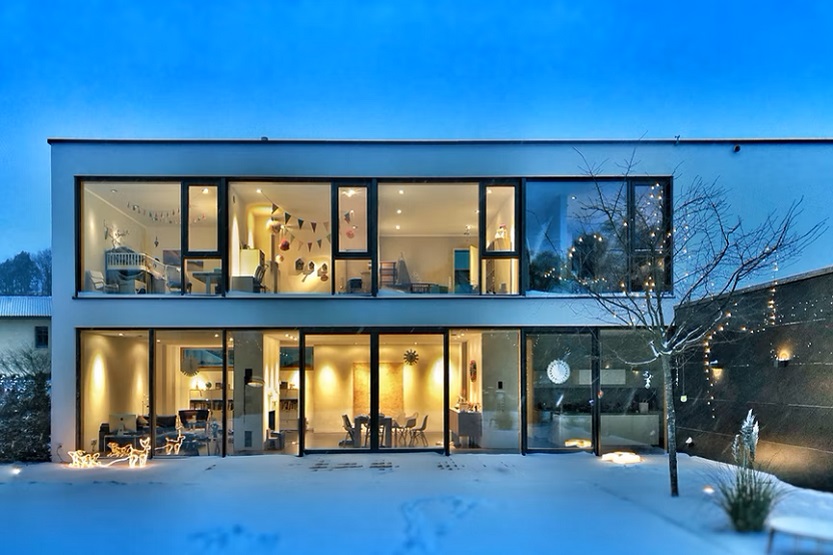 Casa con ventanas de noche y jardín nevado (Stephan Bechert Unsplash)